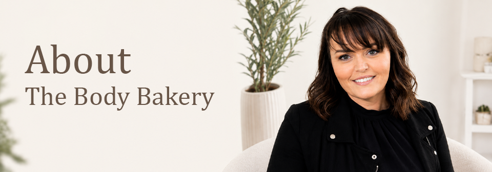 Woman in a black jacket sitting on a white couch with text 'About The Body Bakery' on a light background. About us page. The Body Bakery